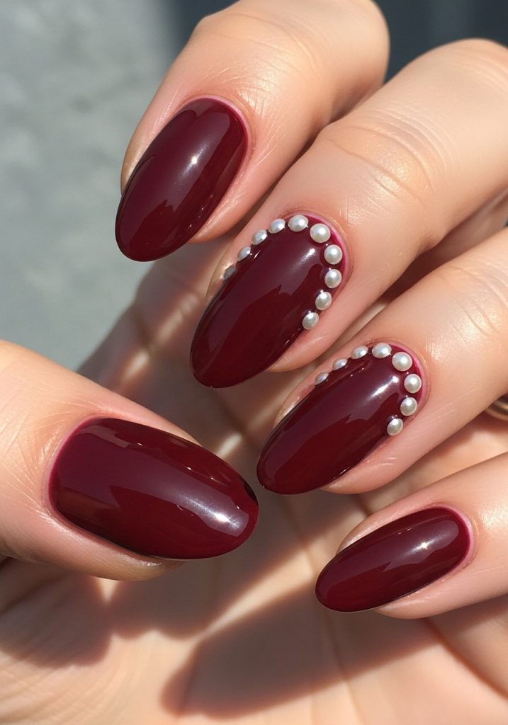 Burgundy nails with small pearl studs near the cuticle on accent fingers