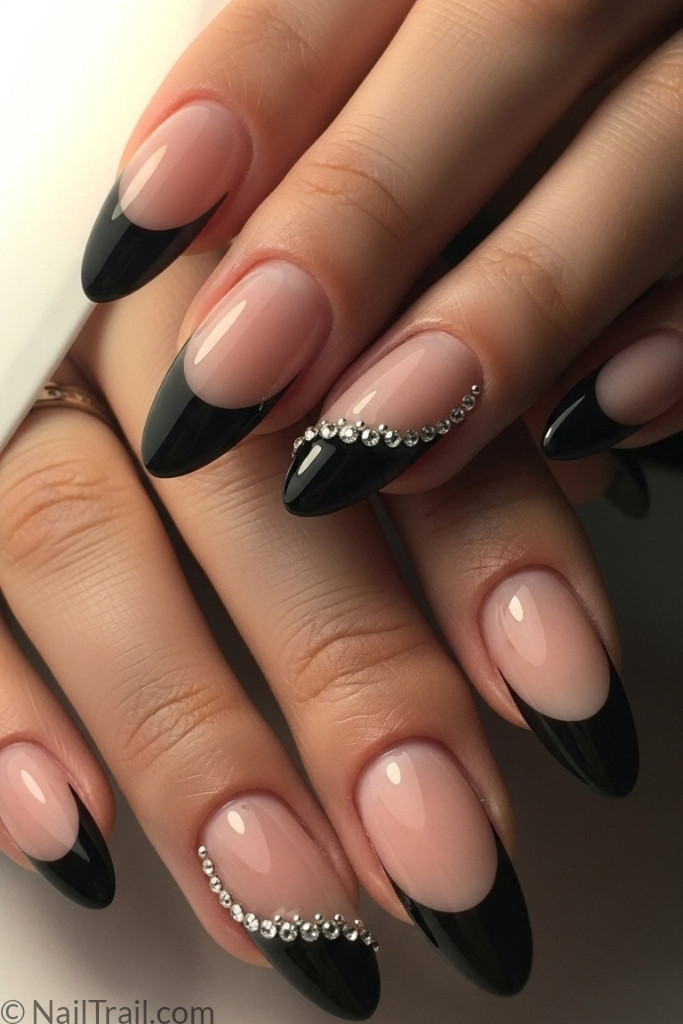 Almond-shaped black French tip nails with rhinestone accents